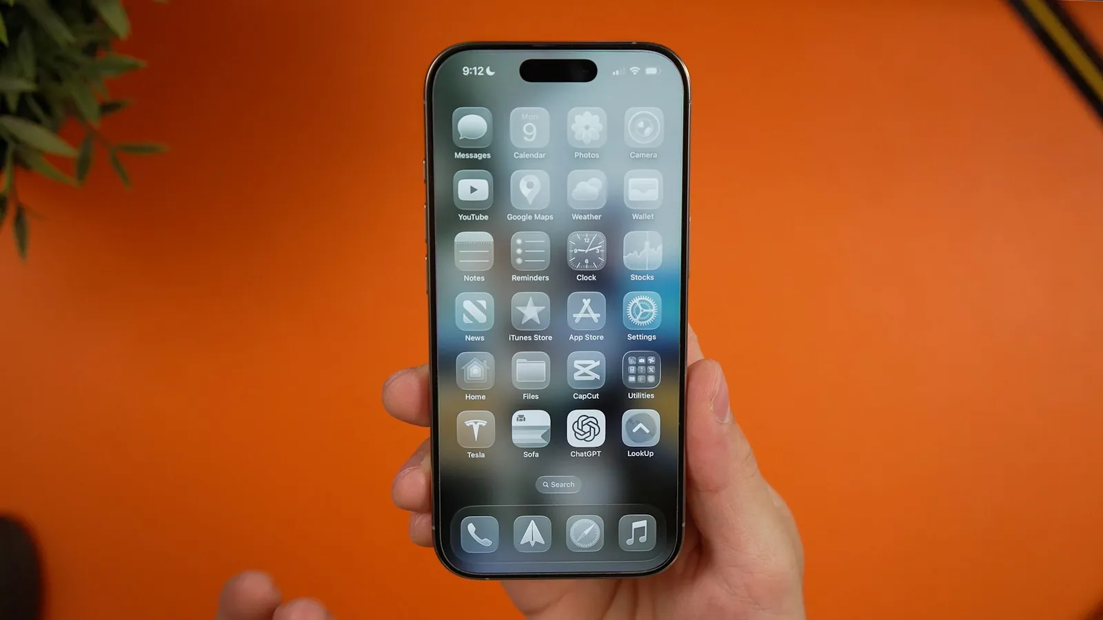 Hand holding an iPhone showing its home screen of apps