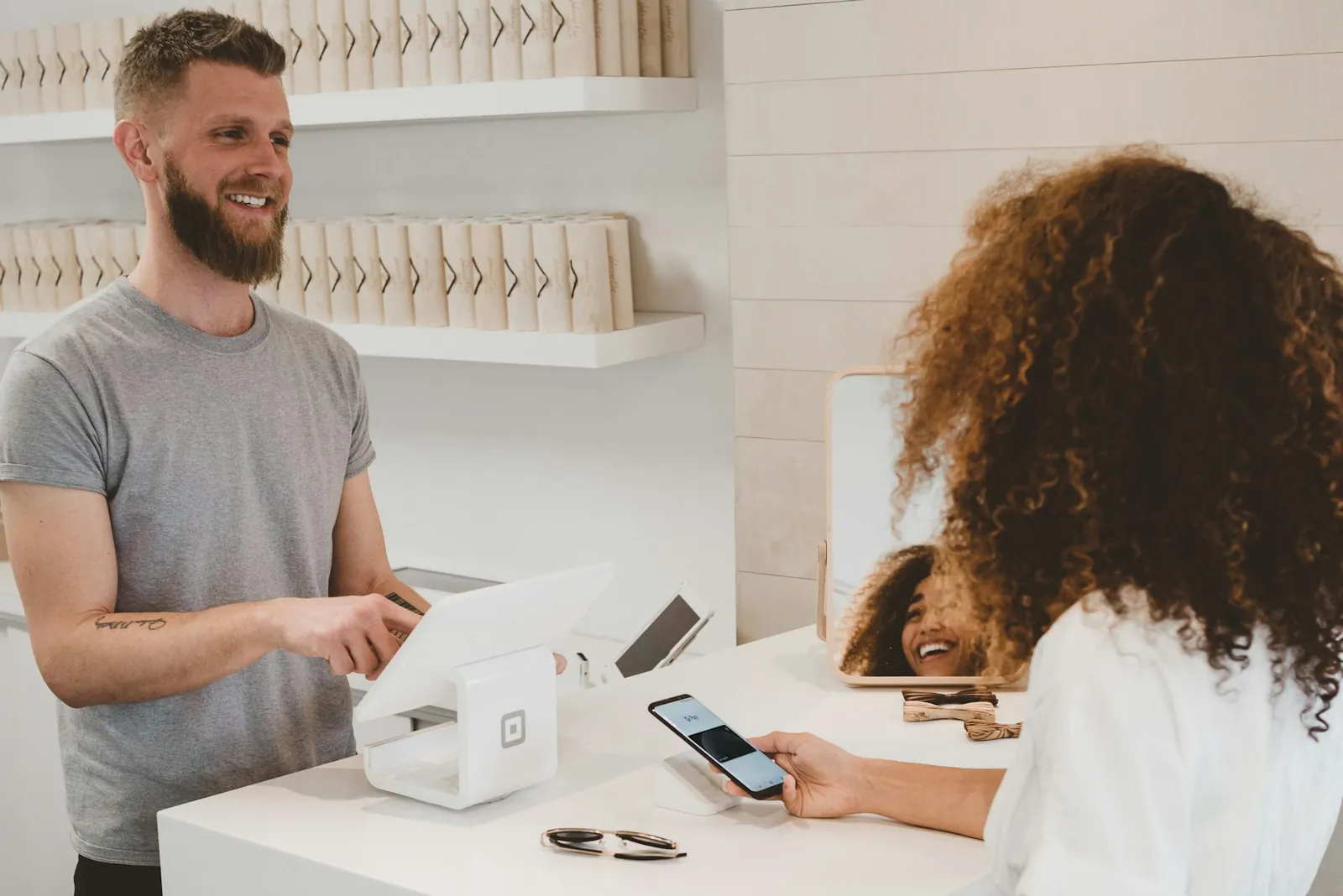 Local shop owner at the counter while a customer pays by phone